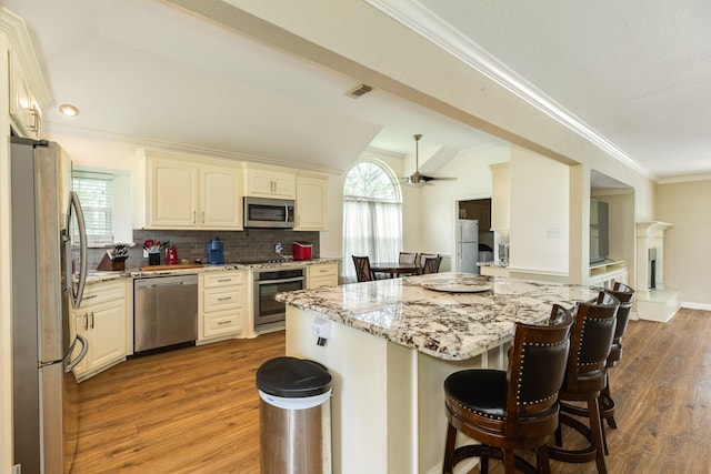 kitchen with wood finished floors, a breakfast bar, stainless steel appliances, light stone countertops, and visible vents
