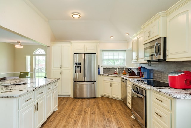 kitchen with tasteful backsplash, light wood-style floors, lofted ceiling, appliances with stainless steel finishes, and light stone countertops