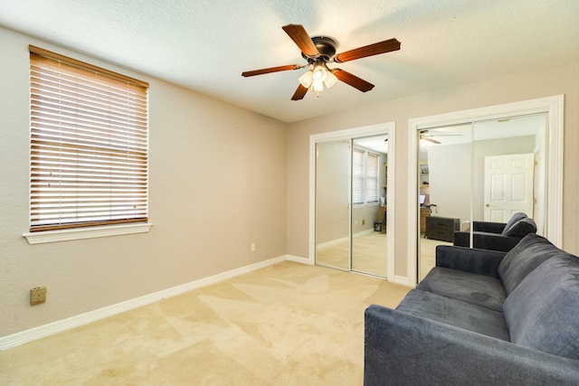 living area with baseboards, a ceiling fan, and light colored carpet