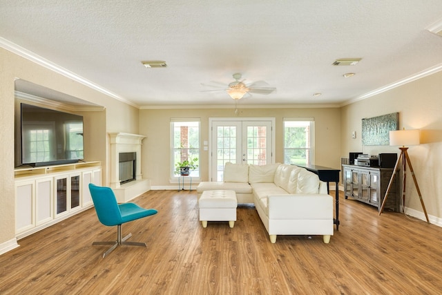 living room with wood finished floors, visible vents, a ceiling fan, crown molding, and baseboards