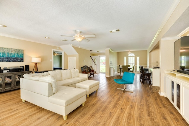 living room featuring light wood-type flooring, ceiling fan, a textured ceiling, and stairway