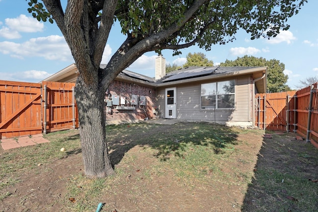 rear view of house featuring a gate, roof mounted solar panels, a chimney, and a fenced backyard
