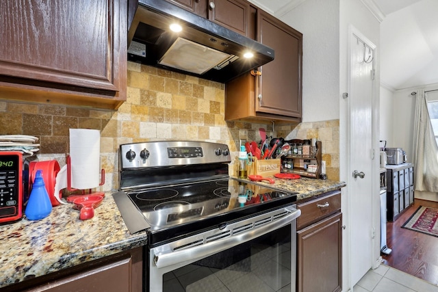 kitchen with stainless steel electric range oven, backsplash, light stone countertops, under cabinet range hood, and light tile patterned floors