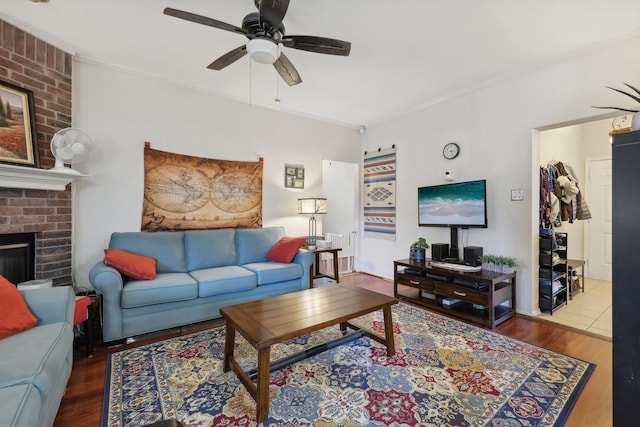living area featuring a brick fireplace, wood finished floors, ceiling fan, and crown molding