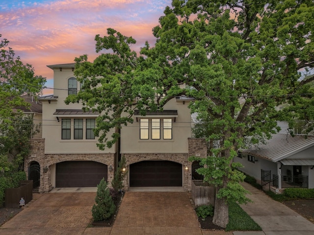 view of property with an attached garage, stone siding, decorative driveway, and stucco siding
