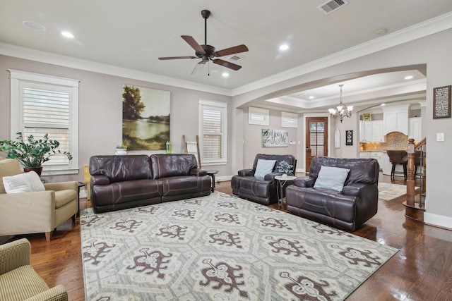 living area featuring arched walkways, a wealth of natural light, ornamental molding, and ceiling fan with notable chandelier