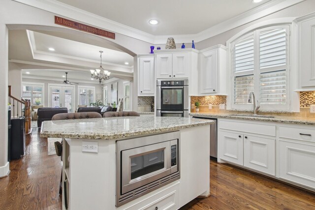 kitchen featuring an inviting chandelier, stainless steel appliances, ornamental molding, a sink, and white cabinetry