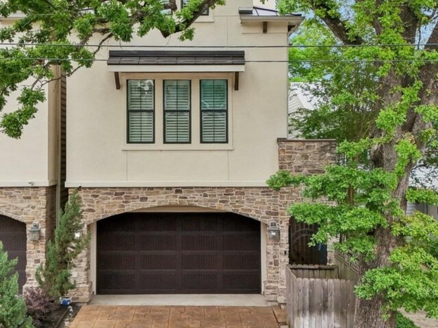 view of side of home featuring a garage, stone siding, concrete driveway, and stucco siding