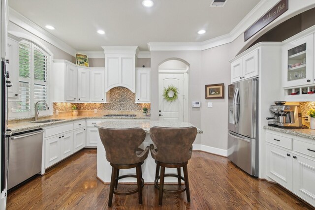 kitchen with stainless steel appliances, backsplash, a sink, crown molding, and white cabinetry