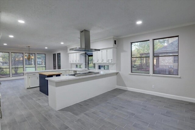 kitchen with a peninsula, island exhaust hood, recessed lighting, white cabinetry, and light countertops