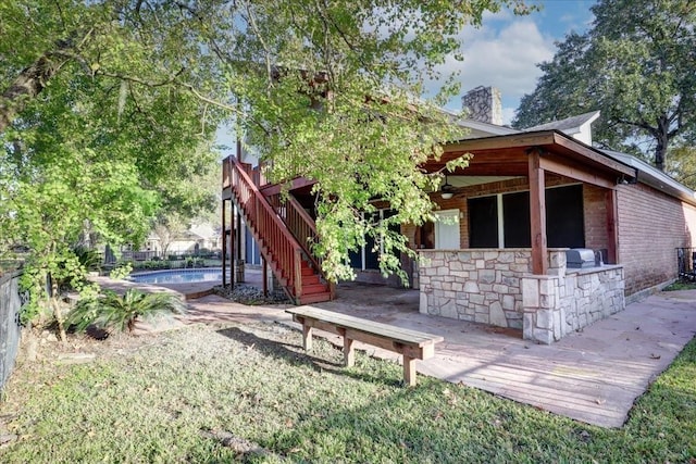 rear view of property featuring stairway, a fenced in pool, ceiling fan, a chimney, and fence