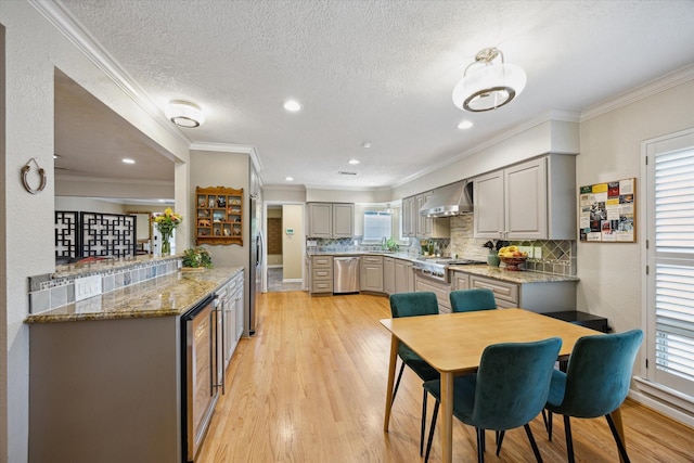 kitchen with wall chimney range hood, light wood-style flooring, gray cabinetry, tasteful backsplash, and appliances with stainless steel finishes