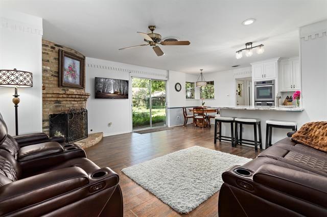 living room with a ceiling fan, a brick fireplace, and dark wood finished floors