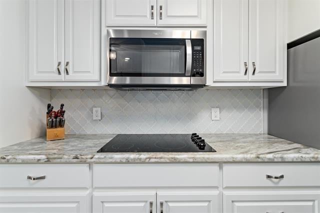 kitchen with stainless steel microwave, black electric stovetop, decorative backsplash, and white cabinets