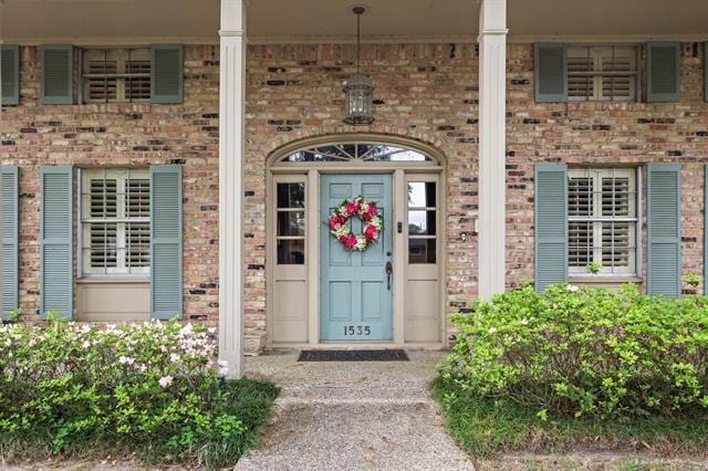view of exterior entry featuring brick siding and a porch