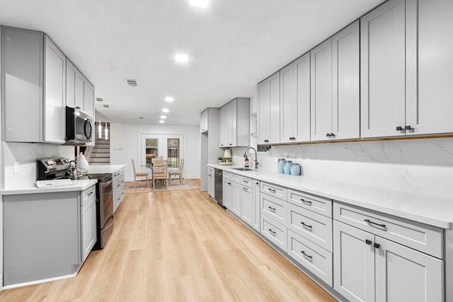 kitchen with stainless steel appliances, light wood-style flooring, a sink, visible vents, and gray cabinetry