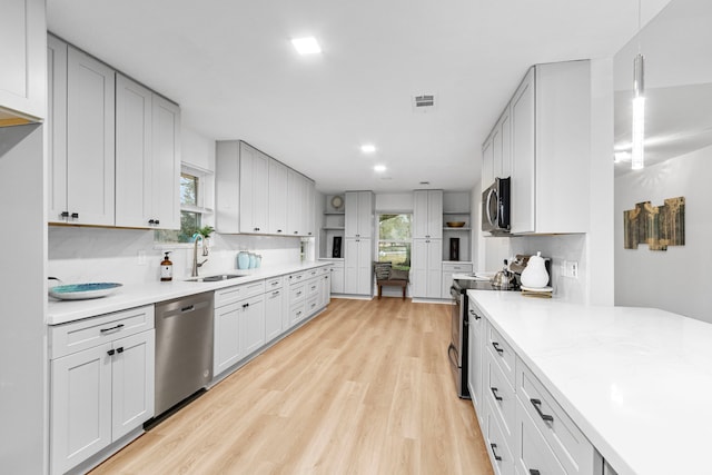 kitchen with appliances with stainless steel finishes, light wood-style flooring, a sink, and light countertops