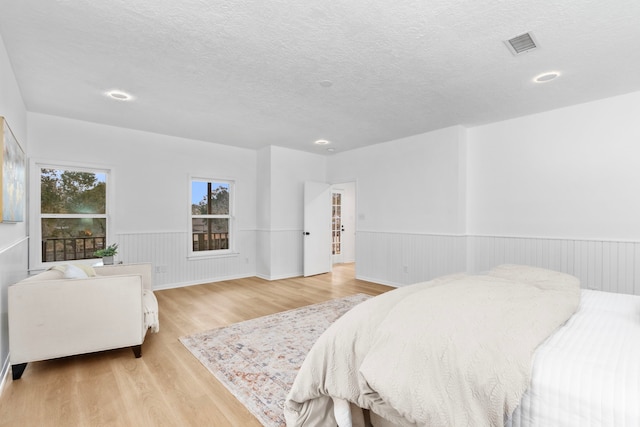 bedroom featuring light wood-style flooring, visible vents, a textured ceiling, and a wainscoted wall