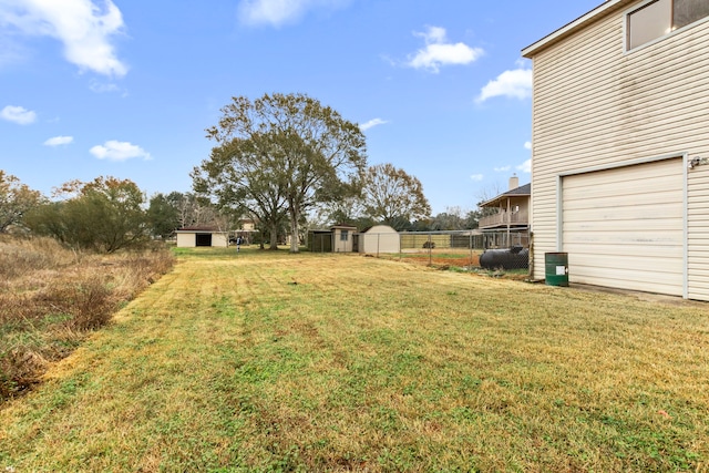 view of yard with a storage shed, an attached garage, fence, and an outdoor structure