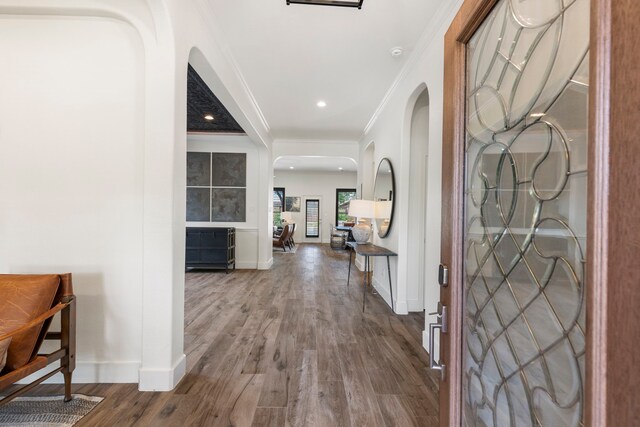 entrance foyer with arched walkways, ornamental molding, baseboards, and wood finished floors
