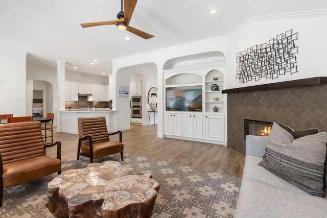 living area with light wood-type flooring, a ceiling fan, a glass covered fireplace, and recessed lighting