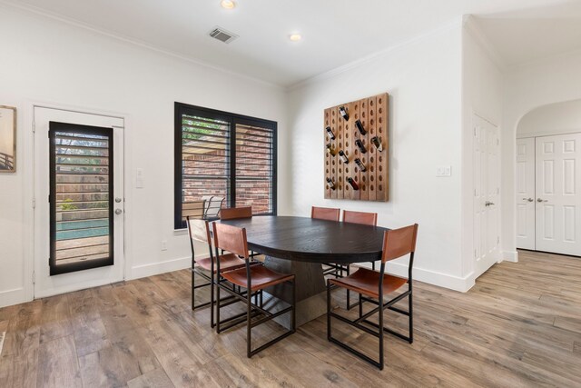 dining room with visible vents, crown molding, light wood-style floors, baseboards, and arched walkways