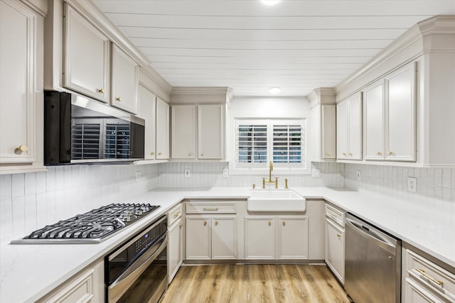 kitchen featuring light wood finished floors, stainless steel appliances, a sink, tasteful backsplash, and light countertops
