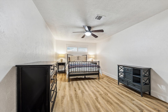 bedroom with a textured wall, visible vents, light wood-style floors, baseboards, and a textured ceiling