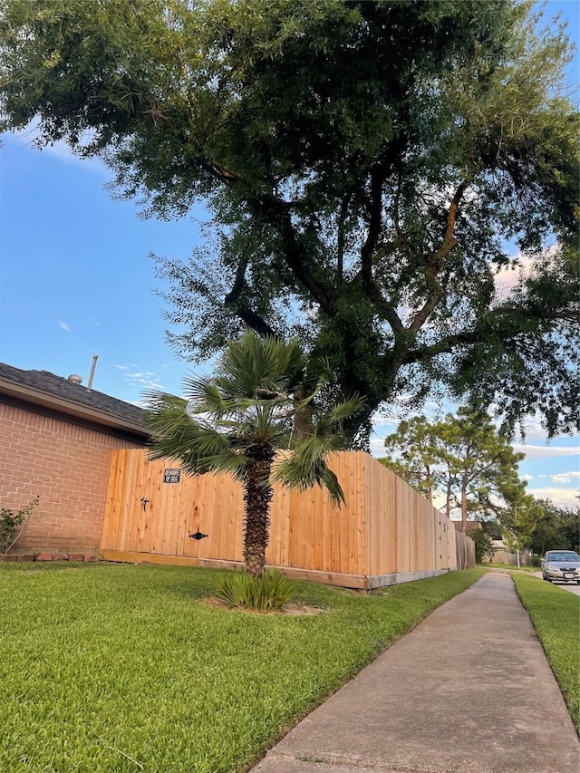 view of side of property featuring a lawn, brick siding, and fence