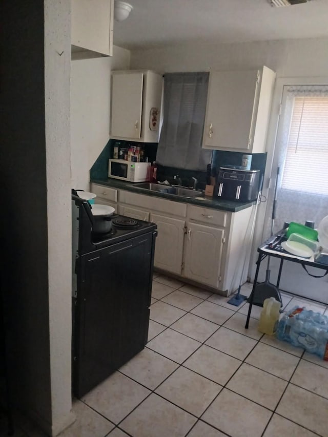 2602 Dalview St, Houston, TX 77091 - kitchen featuring black electric range oven, white microwave, a sink, white cabinetry, and light tile patterned floors