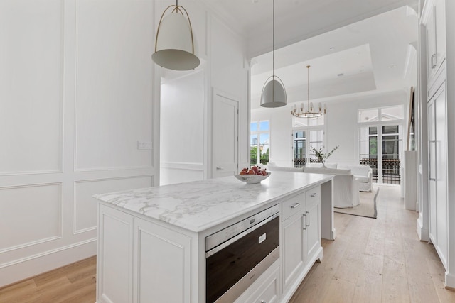 kitchen with white cabinets, stainless steel microwave, light wood-style floors, a decorative wall, and hanging light fixtures