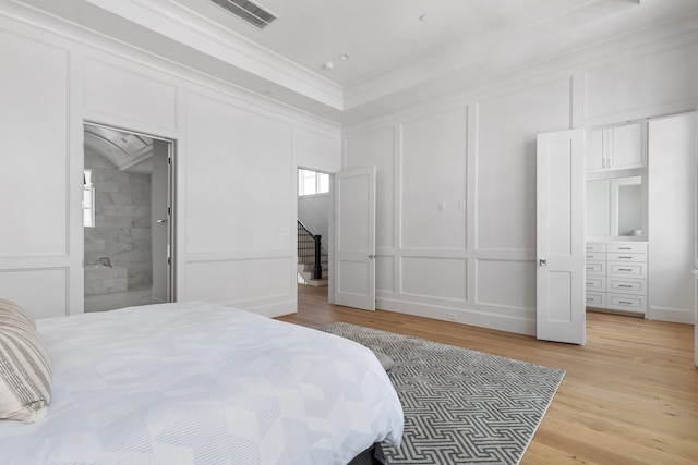 bedroom with a decorative wall, ornamental molding, visible vents, and light wood-type flooring