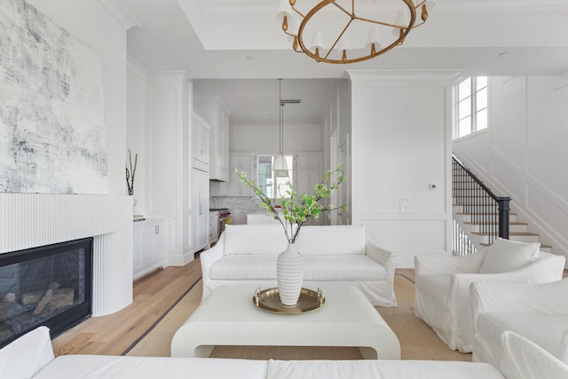 living room with a glass covered fireplace, light wood-type flooring, stairway, and an inviting chandelier