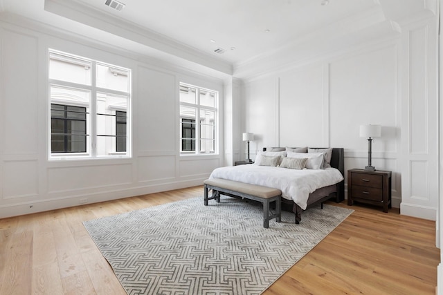 bedroom with crown molding, visible vents, light wood-style floors, and a decorative wall