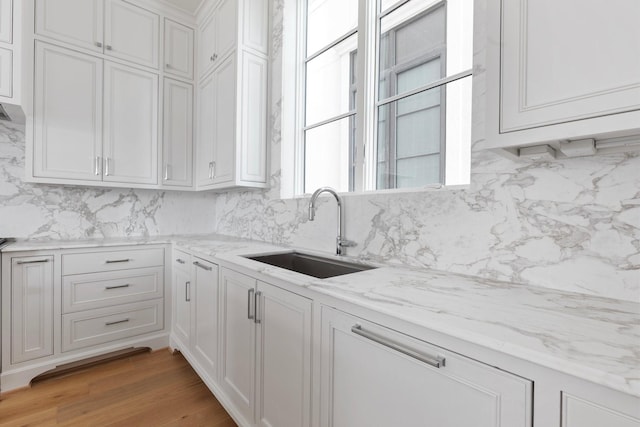 kitchen with decorative backsplash, white cabinetry, light stone countertops, and a sink
