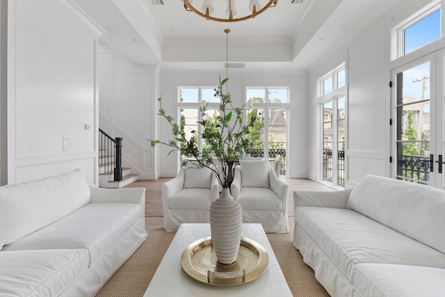 living room with a raised ceiling, an inviting chandelier, stairway, a decorative wall, and ornamental molding