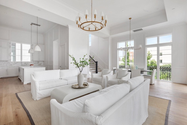 living room featuring an inviting chandelier, visible vents, light wood-style floors, a decorative wall, and stairs