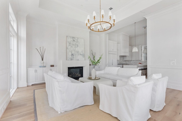 living area with crown molding, a glass covered fireplace, a chandelier, and light wood-style floors