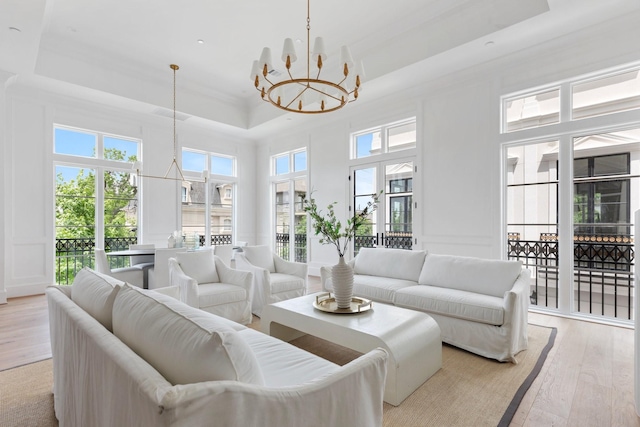 living room featuring a high ceiling, a chandelier, light wood-type flooring, and a raised ceiling