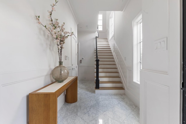staircase with wainscoting, a decorative wall, and ornamental molding