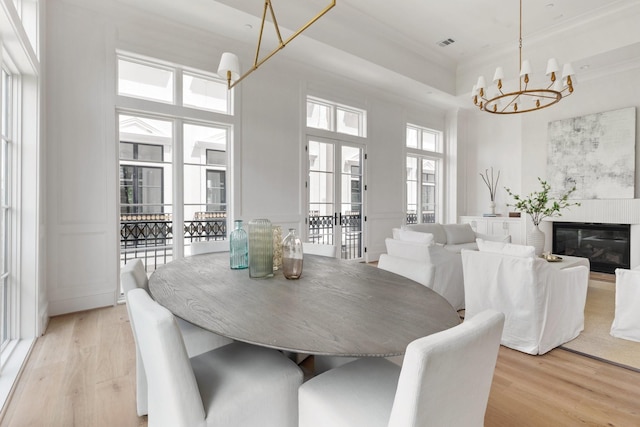 dining room with light wood-style flooring, a towering ceiling, a notable chandelier, and ornamental molding