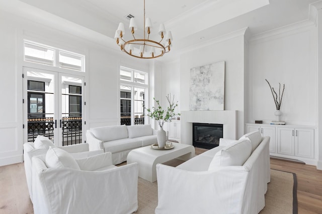 living area with light wood-style flooring, a glass covered fireplace, an inviting chandelier, a decorative wall, and ornamental molding