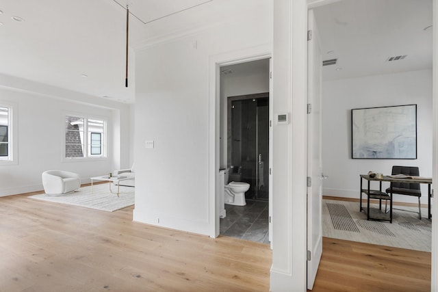 hall with light wood-style floors, visible vents, and baseboards