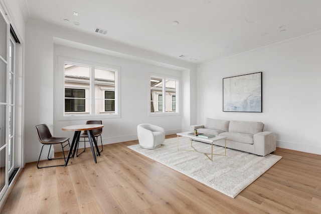living area with light wood-type flooring, visible vents, crown molding, and baseboards