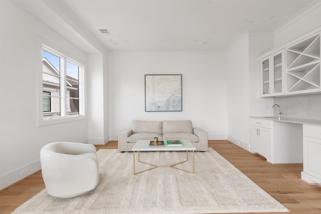 living area with visible vents, crown molding, baseboards, light wood-style flooring, and indoor wet bar