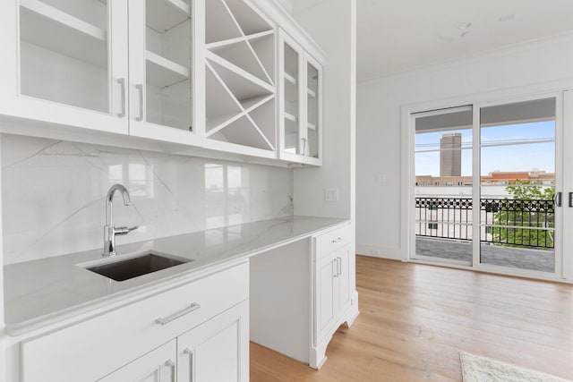 kitchen featuring light wood finished floors, a sink, tasteful backsplash, glass insert cabinets, and light stone countertops