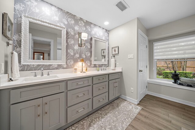 full bath featuring a sink, baseboards, wallpapered walls, wood finished floors, and visible vents