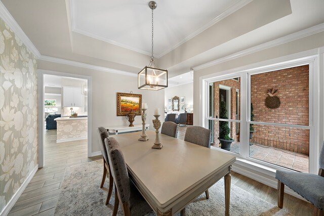 dining room with crown molding, light wood-type flooring, baseboards, an inviting chandelier, and a tray ceiling