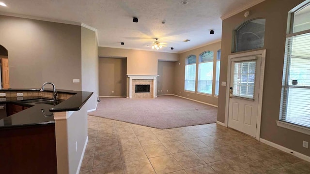 unfurnished living room featuring a sink, ceiling fan, a wealth of natural light, light carpet, and ornamental molding