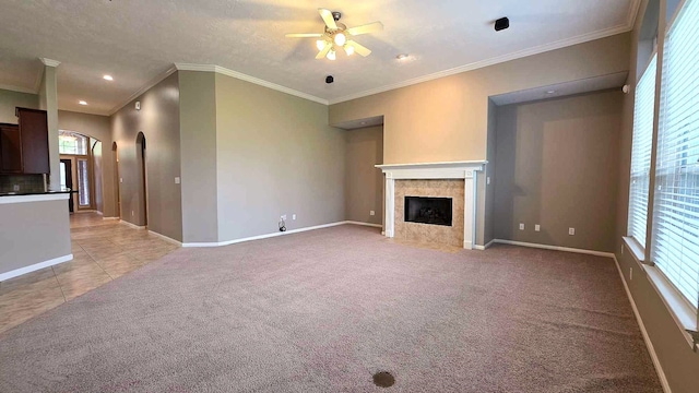 unfurnished living room featuring ornamental molding, a tiled fireplace, a ceiling fan, and a wealth of natural light